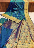 Teal/navy dual tone silk, multi-color mina floral pallu, gold zari border, folded blouse piece layout.
