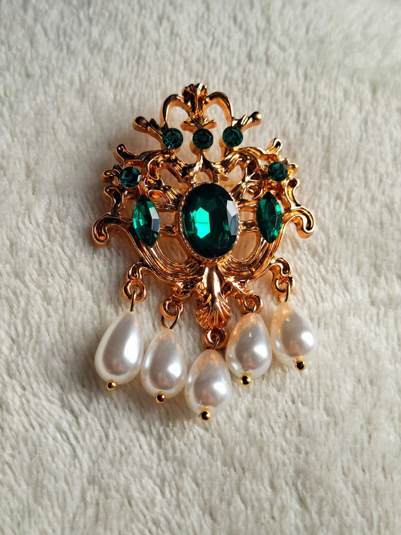  brooch with green stone and pearl-like beads on a textured white background