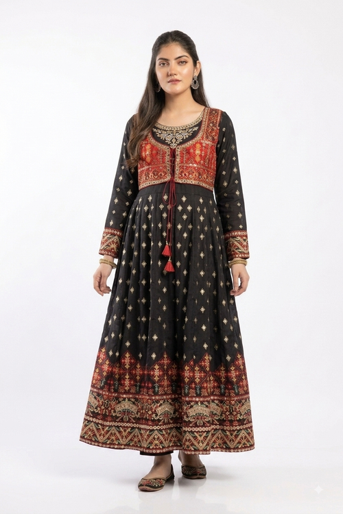 A woman modeling a long black pakistani katan silk Anarkali gown with red and gold traditional patterns, standing against a plain white studio background.