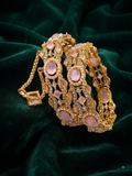 An ornate gold-toned bracelet with multiple pink gemstone accents and clear rhinestone details, displayed on a dark green velvet fabric background.