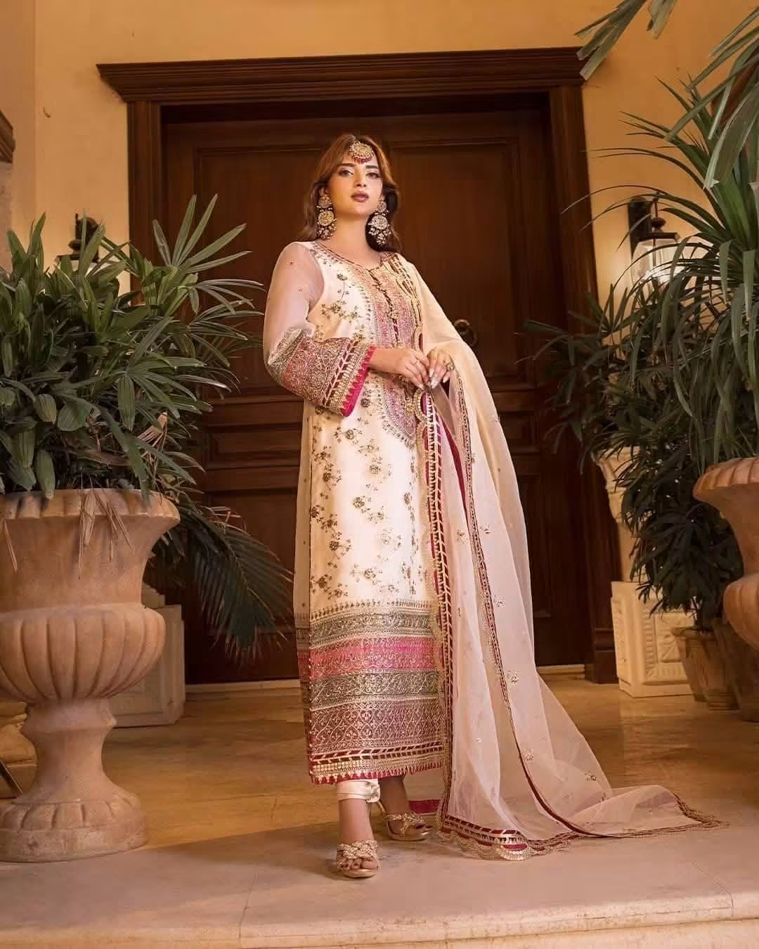 Woman in apakistani organza  traditional outfit in off white or ivory color standing in a room with plants