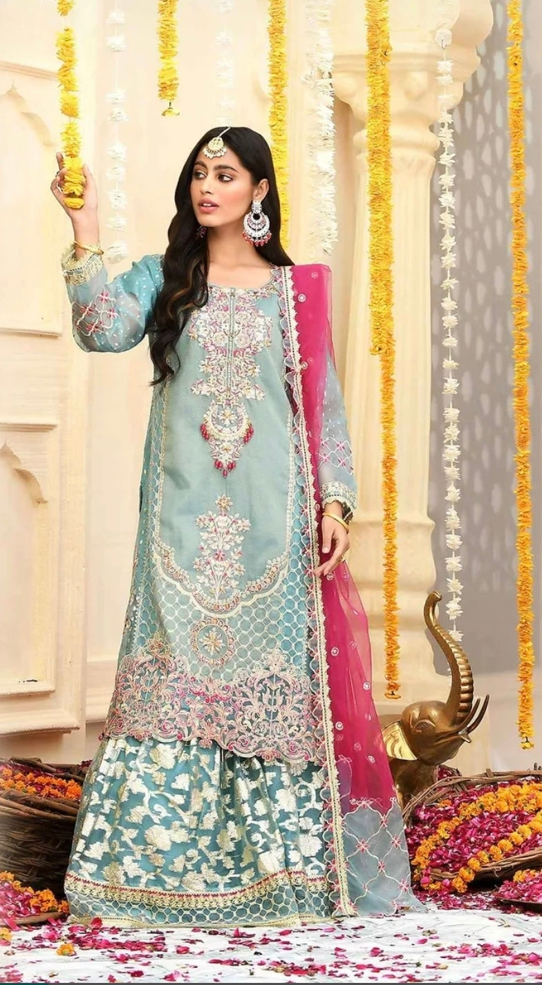 Model wearing a mint green embroidered masoor kurta and matching Banarasi gharara, bright pink dupatta, traditional Indian/Pakistani decor backdrop.