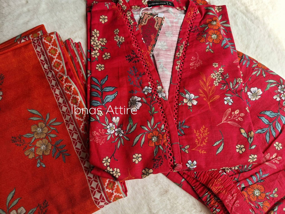 Folded red winter lawn fabric with cream/orange floral prints, Sadabahar brand tags, patterned border dupatta layout.